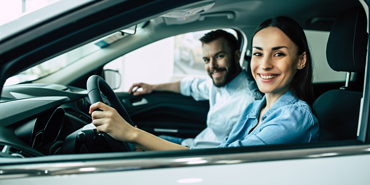 Eine Frau sitzt am Steuer eines Autos, neben ihr sitzt ein Mann. Beide freuen sich über ihr Auto